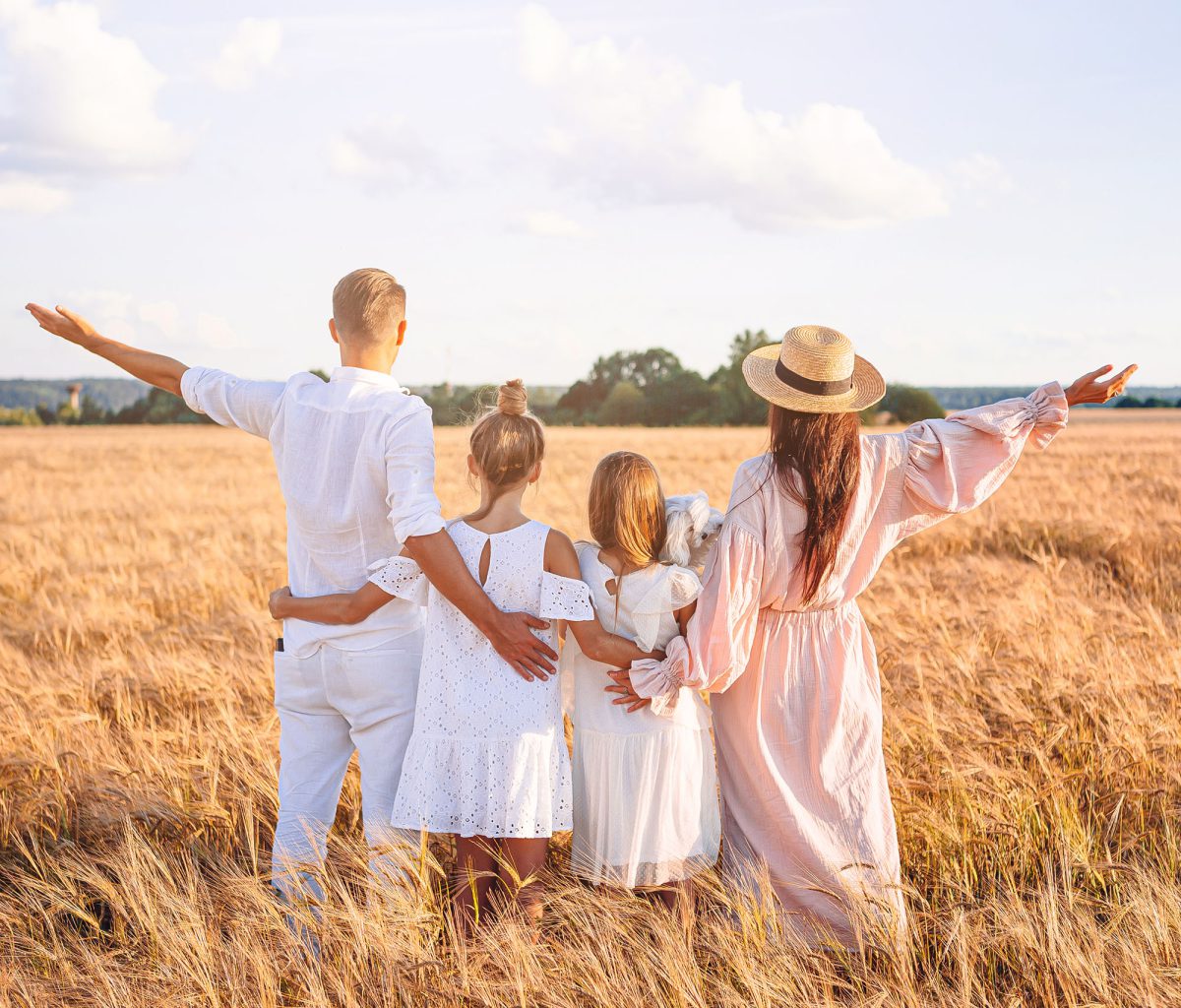 Happy family of four on summer meadow of wheat